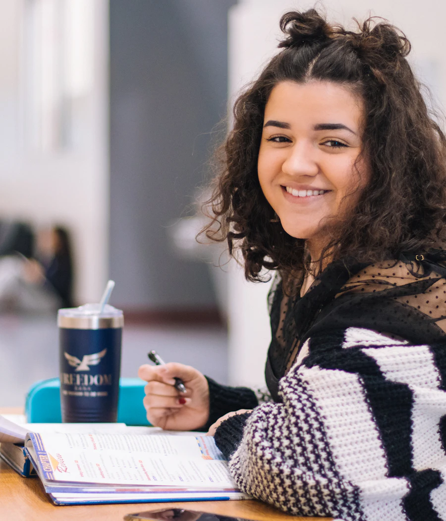 Estudante sorrindo enquanto faz anotações no caderno